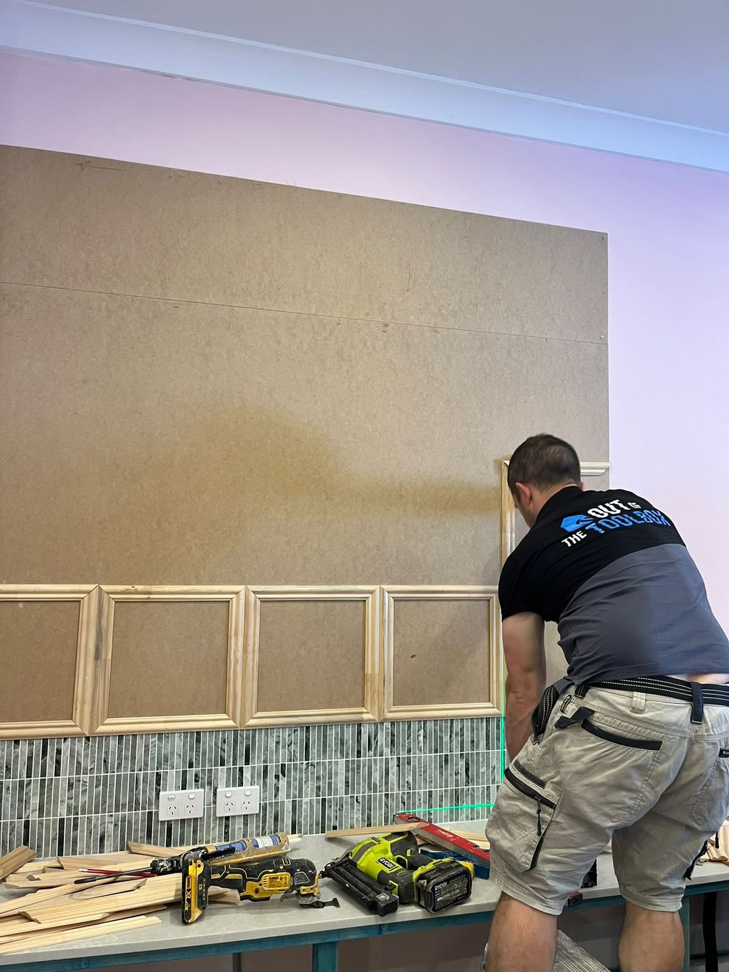 Antonello fixing timber moulding to a feature wall, aligned to a laser line